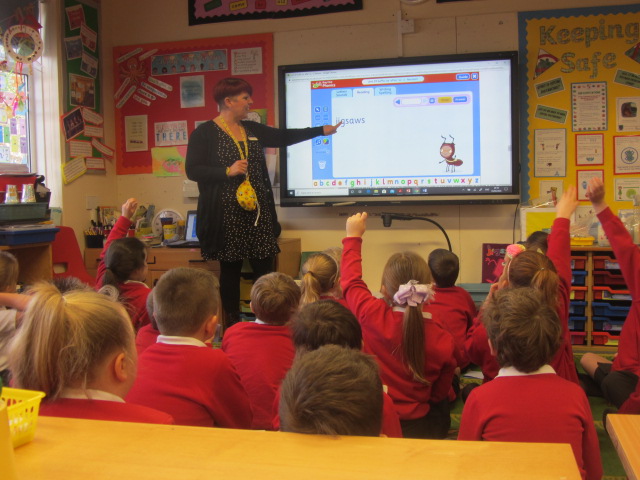 Classroom showing children sitting on the carpet watching the teacher at the front